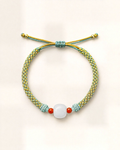 Brote combines a lime-green hand-braided silk cord with a rounded white/grey nephrite jade centre bead and two small orange agate beads.