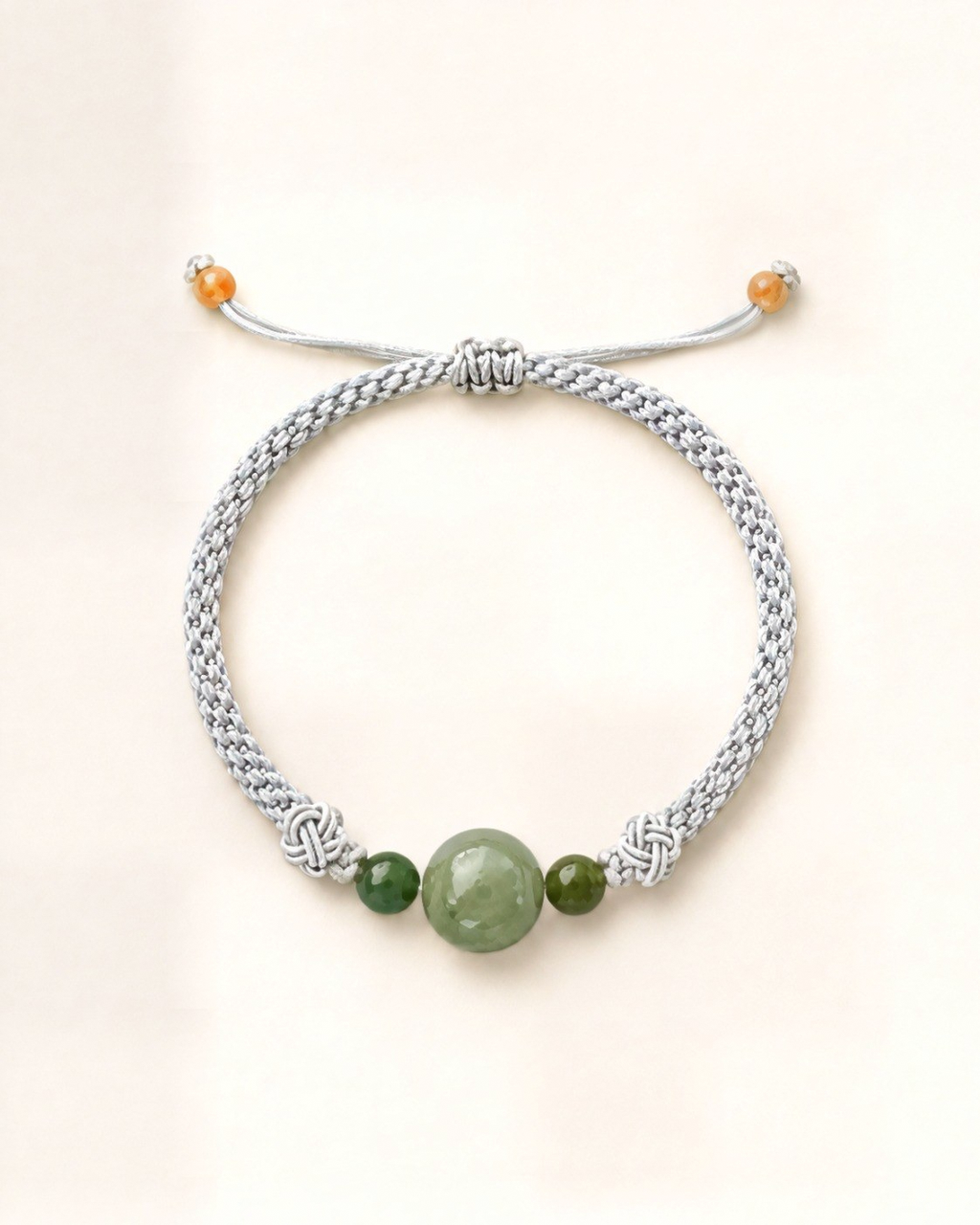 La pulsera Bruma combina un cordón de seda gris claro trenzado a mano con tres cuentas de jade nefrita verde de distinto tamaño.