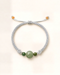 La pulsera Bruma combina un cordón de seda gris claro trenzado a mano con tres cuentas de jade nefrita verde de distinto tamaño.