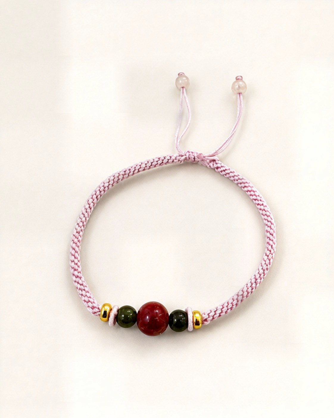 Cereza pairs a pale pink hand-braided silk cord with a red agate centre bead and two dark green nephrite jade beads.