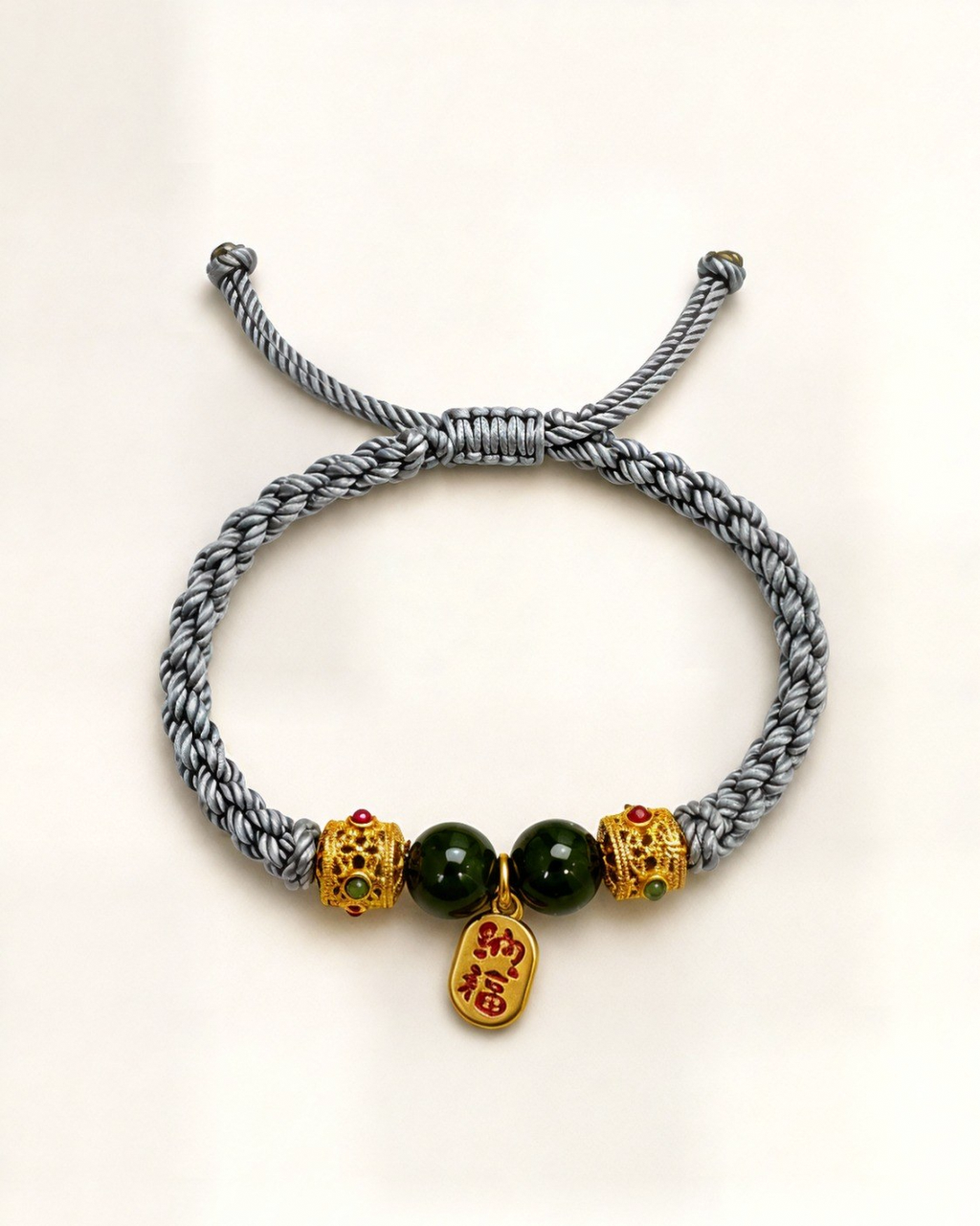 Jardín Dorado combines a grey hand-braided silk cord, two green nephrite jade beads and gold-plated bronze ornaments with coloured details.