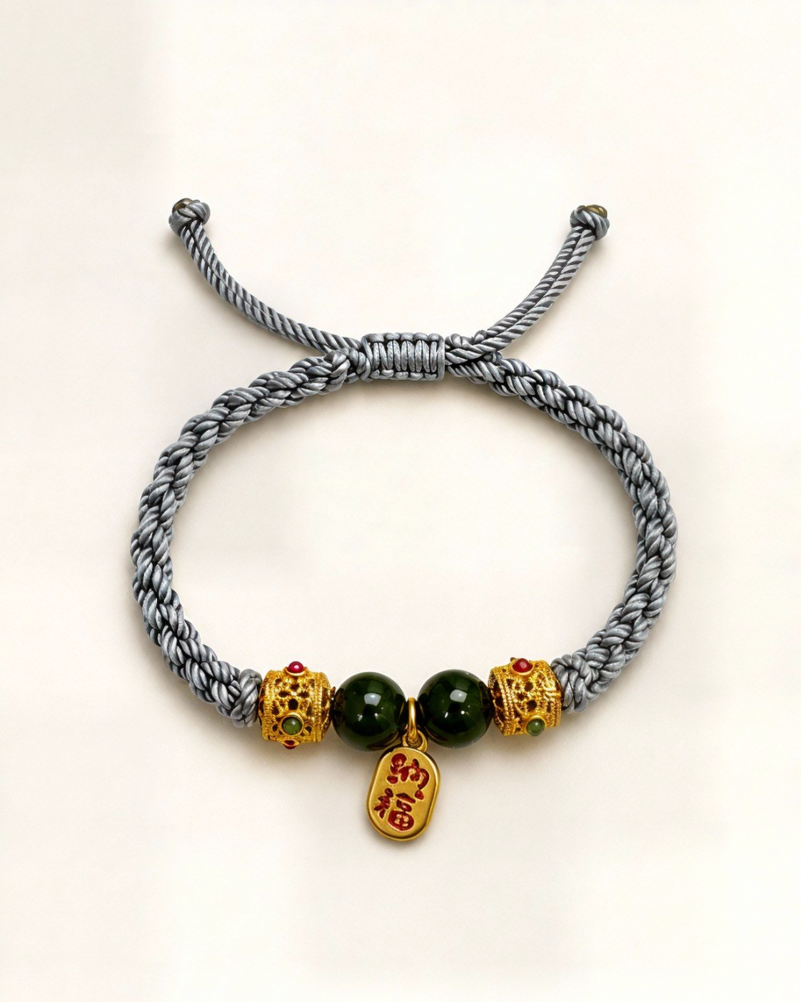 Jardín Dorado combines a grey hand-braided silk cord, two green nephrite jade beads and gold-plated bronze ornaments with coloured details.