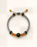 Otoño pairs a grey hand-braided silk cord with a dark green nephrite jade centre bead and smaller honey-orange agate beads.