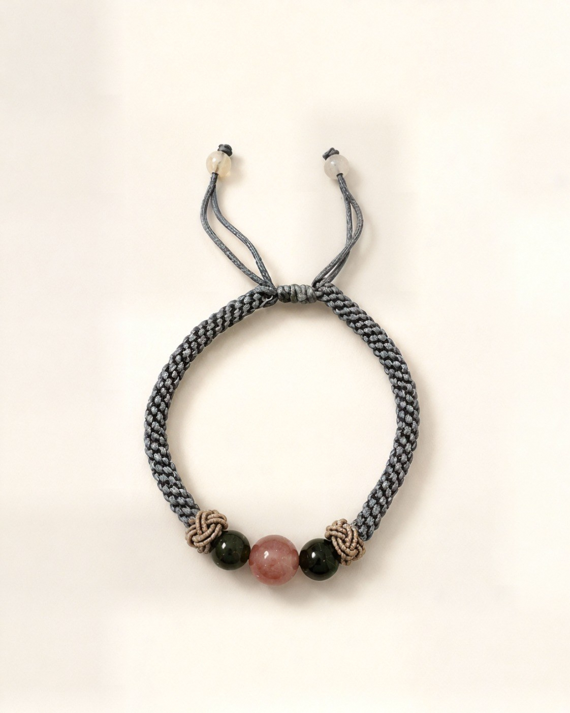 Rocío combines a grey hand-braided silk cord, a pink agate centre bead and two dark green nephrite jade beads.